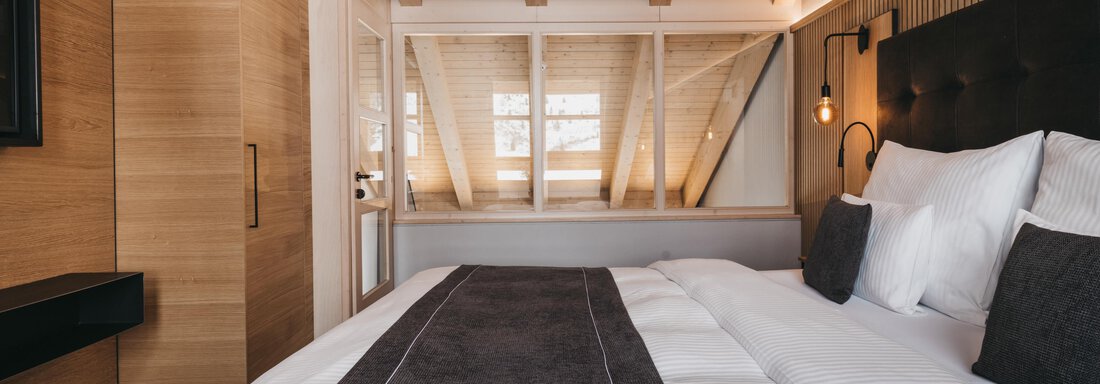 A modern bedroom with a large bed and stylish wood design. The warm colors and natural light create an inviting atmosphere. - The Crystal VAYA Unique - Obergurgl 