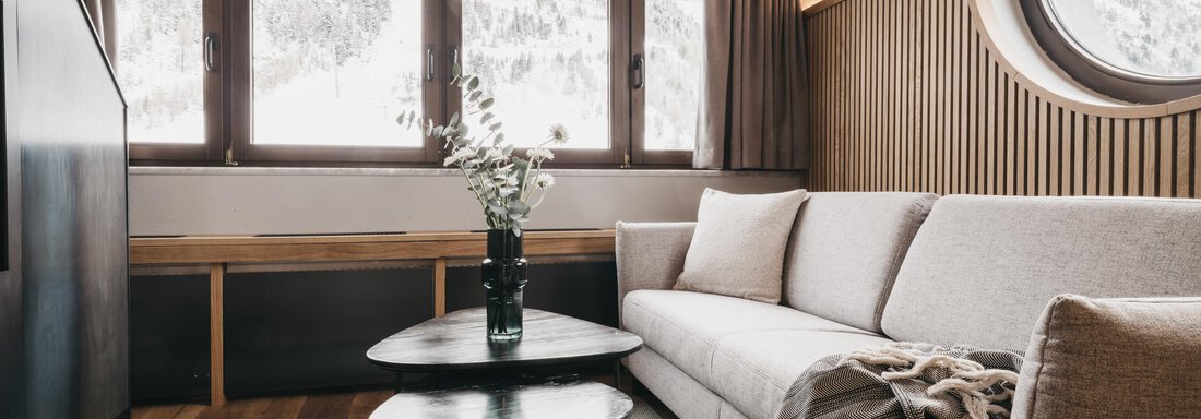 Maisonette Suite | © The Crystal VAYA Unique (CC C) A modern living room with a bright couch and a low table. Large windows provide a view of the mountain landscape. - The Crystal VAYA Unique - Obergurgl