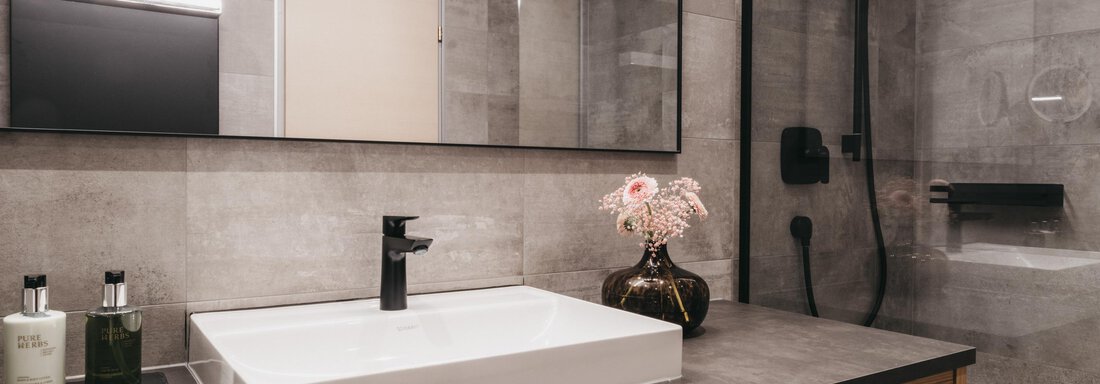 A modern bathroom with a simple washbasin and elegant wooden shelf. The walls are in neutral gray tones and decorated with stylish accessories. - The Crystal VAYA Unique - Obergurgl 