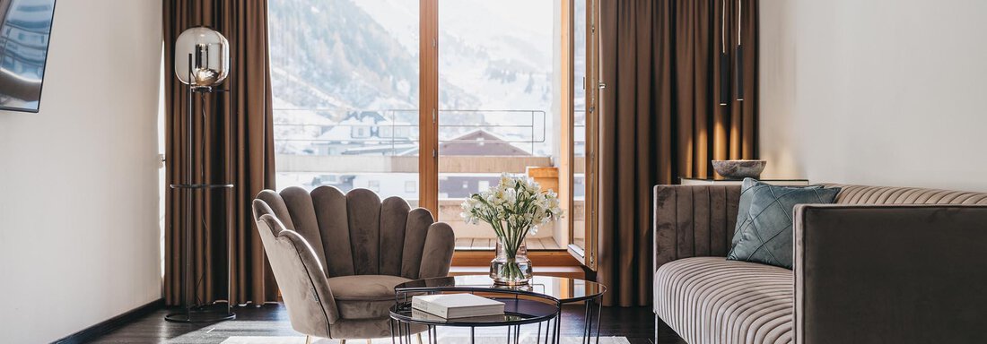 VAYA The Crystal A stylish living room with a comfortable armchair and an elegant sofa. Large windows offer a view of the mountains and let in plenty of light. - The Crystal VAYA Unique - Obergurgl