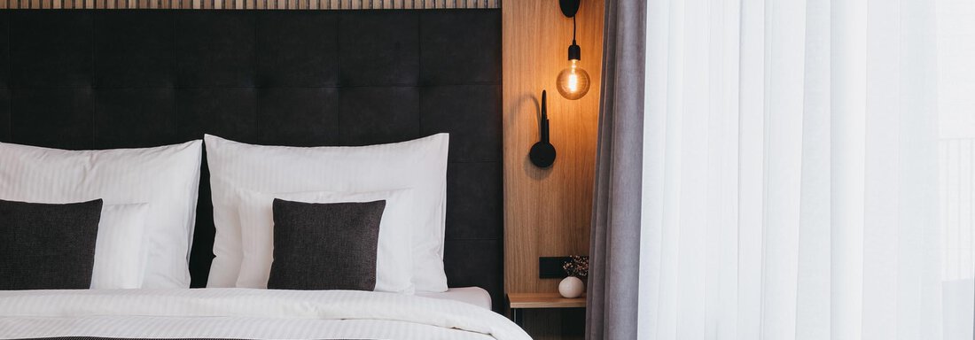A modern bedroom with a comfortable bed and elegant pillows. The large windows let in plenty of daylight, creating an inviting atmosphere. - The Crystal VAYA Unique - Obergurgl 