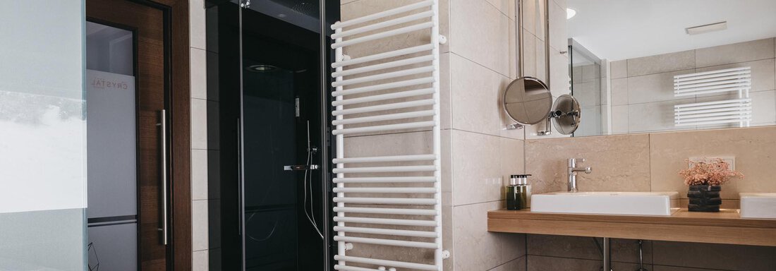 A modern bathroom with a freestanding bathtub and a shower. The walls are brightly tiled and there is a wooden shelf with towels. - The Crystal VAYA Unique - Obergurgl 