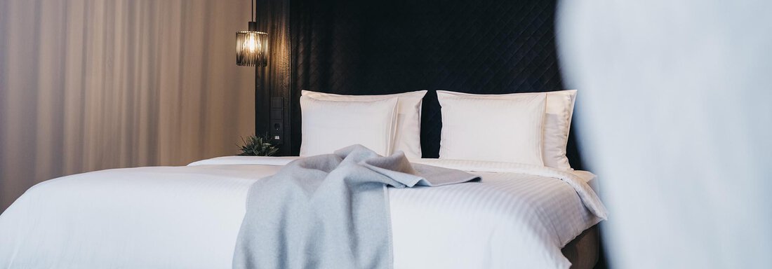 A modern bedroom with a large double bed and white bedding. A gray blanket casually drapes over the bed, and the walls are painted in soft colors. - The Crystal VAYA Unique - Obergurgl 