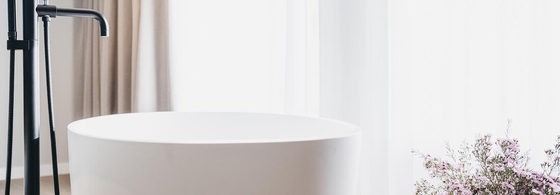 A modern bathroom with an elegant, freestanding bathtub. Next to the tub is a black vase with fresh flowers. - The Crystal VAYA Unique - Obergurgl 