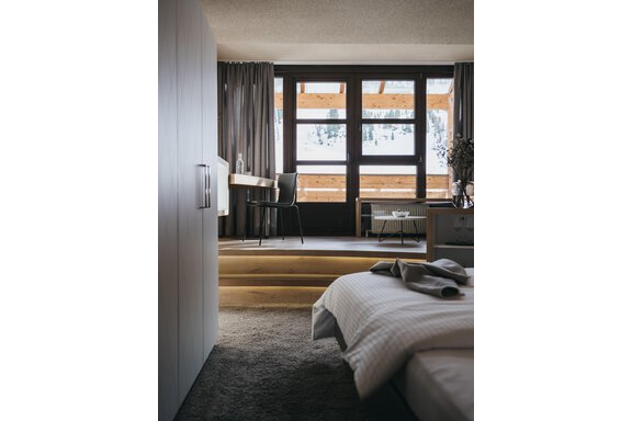 VAYA The Crystal-90 (1) A modern bedroom with a large window and a view of a terrace. The room is stylishly furnished with a desk and a cozy bed. - The Crystal VAYA Unique - Obergurgl