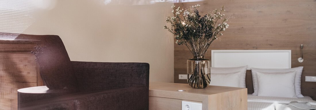 A modern room with wooden wall and minimalist decor. On a table, there is a bowl of snacks and a bouquet of flowers. - The Crystal VAYA Unique - Obergurgl 
