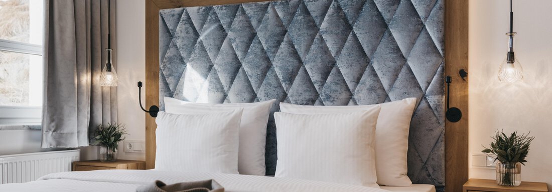 A modern bedroom with a upholstered headboard and two white pillows. The room design is bright and inviting, with plants and stylish light sources. - The Crystal VAYA Unique - Obergurgl 