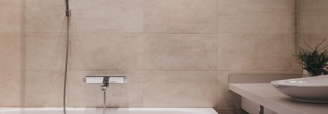A modern bathroom with a white bathtub and a minimalist faucet. The walls are tiled with light tiles and there is an elegant sink area. - The Crystal VAYA Unique - Obergurgl 