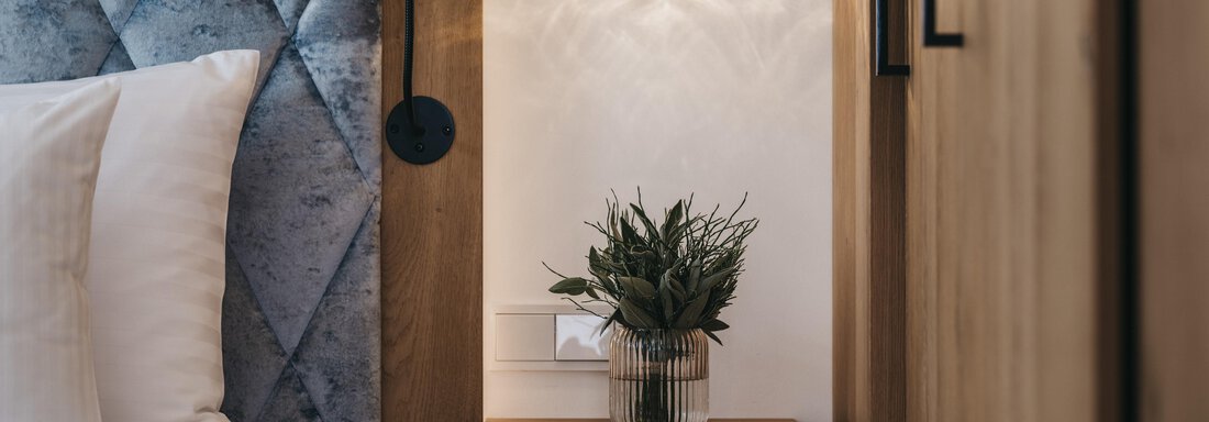 A modern bedroom with a stylish bedside table and a plant. A cozy lamp hangs on the wall above the bed. - The Crystal VAYA Unique - Obergurgl 
