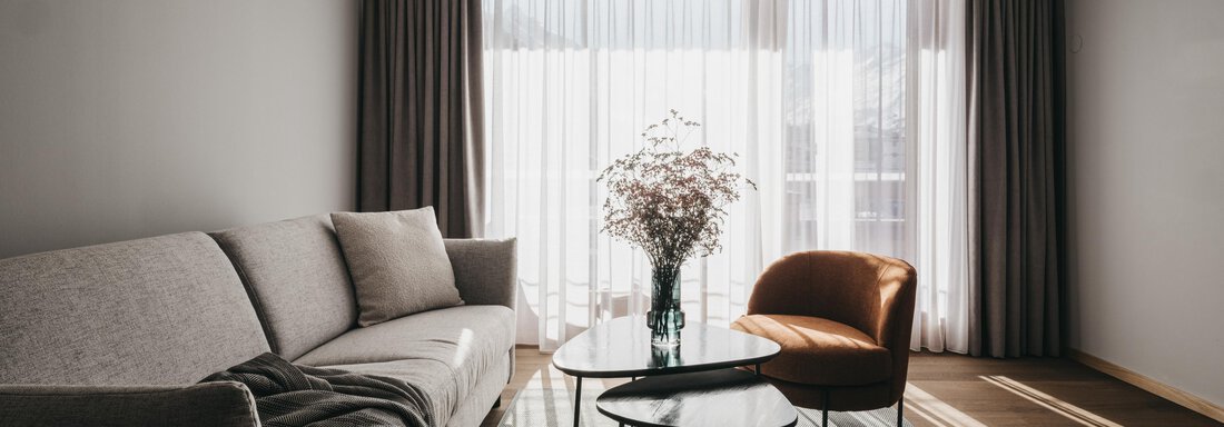 Grand Deluxe Suite A modern living room with a grey sofa and a cozy armchair. Large windows let in plenty of daylight, and decorative plants create a pleasant atmosphere. - The Crystal VAYA Unique - Obergurgl