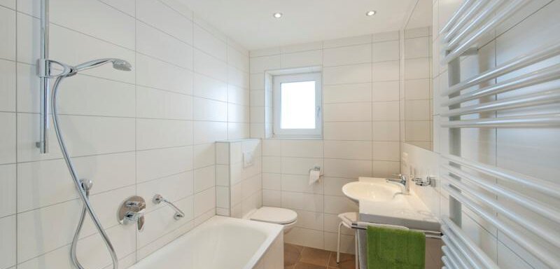 Ein modernes Badezimmer mit einer Badewanne, Dusche und Waschbecken. Helle, weiße Fliesen und ein Fenster sorgen für eine freundliche Atmosphäre. - Pension Michael - Obergurgl 