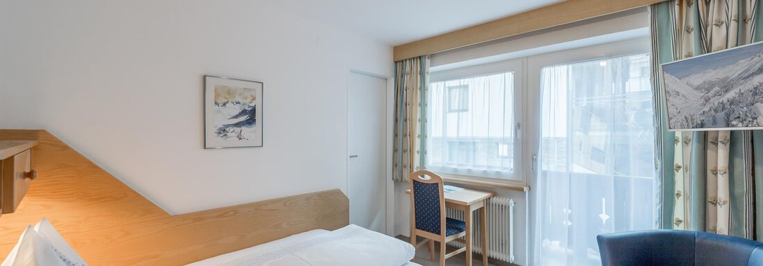 Ein einfaches Zimmer mit einem Einzelbett, einem blauen Sessel und einem Schreibtisch. Große Fenster sorgen für viel Tageslicht. - Pension Michael - Obergurgl 