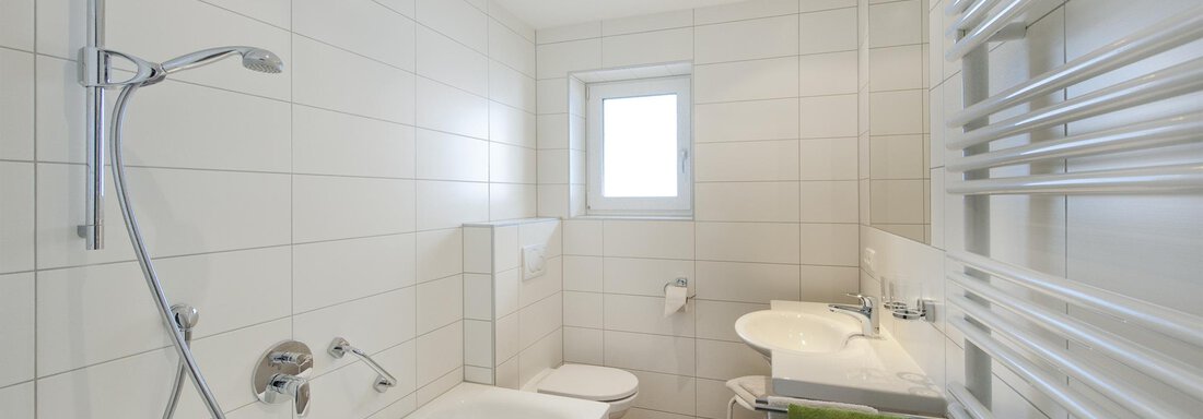 Ein modernes Badezimmer mit einer Badewanne, Dusche und einem Waschbecken. Es gibt helle Fliesen und ein Fenster, das natürliches Licht hereinlässt. - Pension Michael - Obergurgl 
