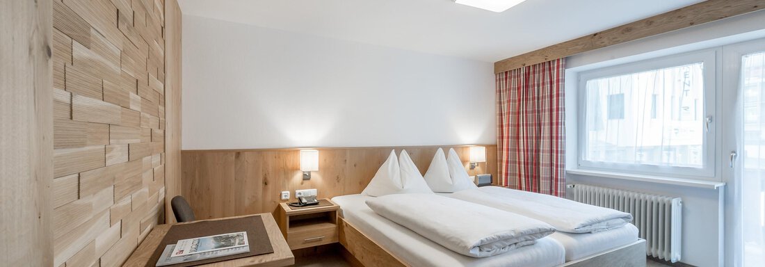 Ein gemütliches Schlafzimmer mit einem Holzwand-Design und zwei Betten. Große Fenster lassen viel Tageslicht herein. - Pension Michael - Obergurgl 