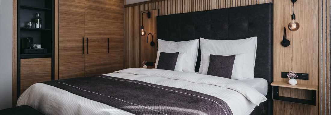 Deluxe Room I | © The Crystal VAYA Unique (CC C) A modern bedroom with a large bed and elegant wood paneling. The warm colors and minimalist furniture create a cozy atmosphere. - The Crystal VAYA Unique - Obergurgl