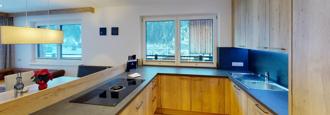 Rubin-Studio-12-Kitchen (1) Eine moderne Küche mit Holzschränken und einer schlichten Arbeitsfläche. Große Fenster sorgen für viel natürliches Licht. - A CASA "Rubin Chalet & Studio Resort" - Sölden