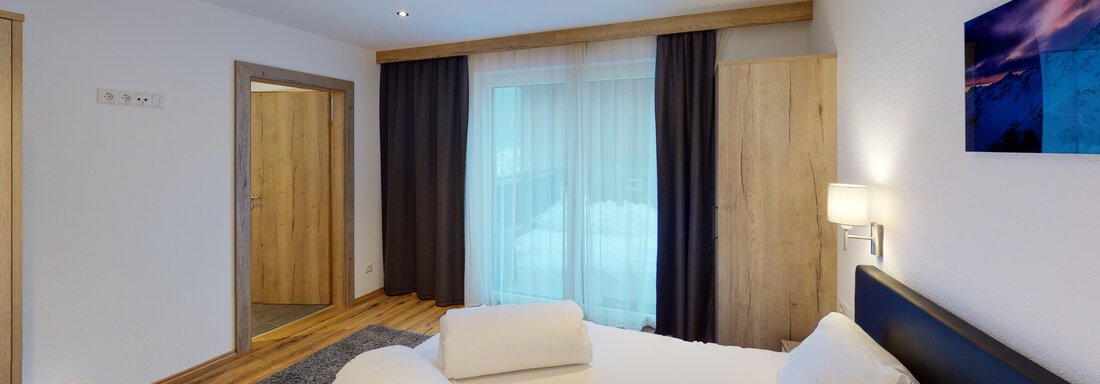 Ein modernes Schlafzimmer mit einem großen Bett und hellen Holzdetails. Große Fenster lassen viel Licht herein und bieten Zugang zu einem Balkon. - A CASA "Rubin Chalet & Studio Resort" - Sölden