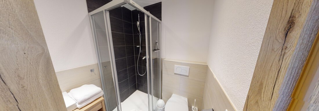 Ein modernes Badezimmer mit einer Dusche, einem WC und einem Holzregal. Die Raumgestaltung ist schlicht und funktional. - A CASA "Rubin Chalet & Studio Resort" - Sölden