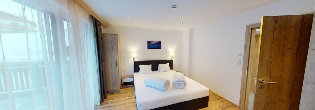 Ein modernes Schlafzimmer mit einem Doppelbett und großen Fenstern. Der Raum ist freundlich und hell, mit Holzfußboden und einfachen Möbeln. - A CASA "Rubin Chalet & Studio Resort" - Sölden