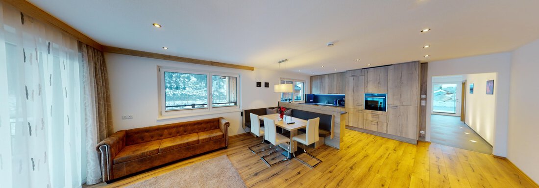 Ein modern gestaltetes Wohnzimmer mit Holzfußboden und viel natürlichem Licht. Es gibt eine gemütliche Couch, einen Esstisch und eine offene Küche im Hintergrund. - A CASA "Rubin Chalet & Studio Resort" - Sölden