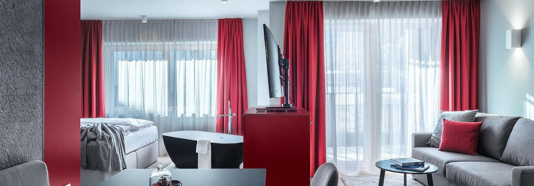 Eine moderne Wohnung mit roten Vorhängen und einem gemütlichen Wohnbereich. Der Raum ist hell und einladend, mit einem Essbereich und einer großen Fensterfront. - AlpenParks The Secret Sölden - Sölden