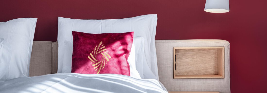 Ein modernes Schlafzimmer mit einem roten Wandverkleidung und einem gemütlichen Bett. Auf dem Nachttisch steht eine Lampe und ein dekorisches Kissen. - AlpenParks The Secret Sölden - Sölden
