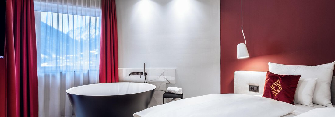 Ein modernes Hotelzimmer mit einem großen Bett und einem eleganten Badezimmer. Die Wände sind teilweise rot und es gibt viel natürliches Licht durch das Fenster. - AlpenParks The Secret Sölden - Sölden