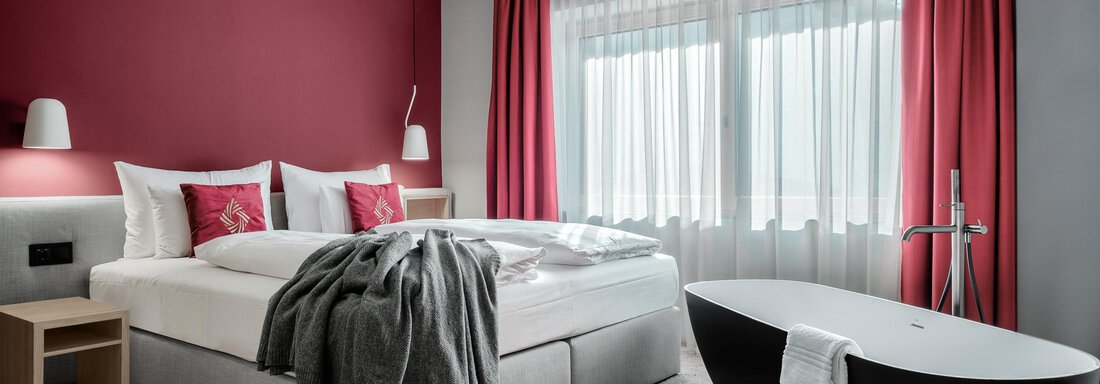Apartment-resort-im-oetztal -the-secret-soelden-si Ein modernes Hotelzimmer mit einem großen Bett und einem eleganten Badezimmer. Die Wände sind rot gestrichen und es gibt helle Vorhänge, die viel Licht hereinlassen. - AlpenParks The Secret Sölden - Sölden