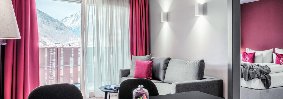 Ein modernes Wohnzimmer mit einem großen Fenster und schöner Aussicht auf die Berge. Die Einrichtung ist elegant mit roten Vorhängen und gemütlichen Möbeln. - AlpenParks The Secret Sölden - Sölden