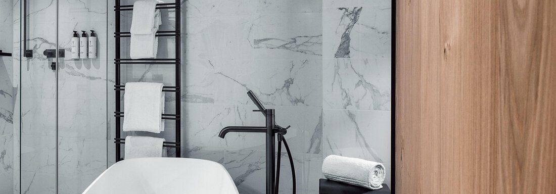 Ein modernes Badezimmer mit einer freistehenden Badewanne in Schwarz und Weiß. Elegante Fliesenwände und eine stilvolle Dusche ergänzen das Design. - AlpenParks The Secret Sölden - Sölden