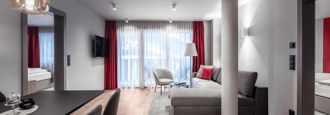 Ein modernes Wohn- und Esszimmer mit einem eleganten Sofa und einem Tisch. Große Fenster sorgen für viel Tageslicht und eine helle, einladende Atmosphäre. - AlpenParks The Secret Sölden - Sölden