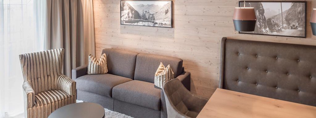 Ein modernes Wohnzimmer mit einem gemütlichen Sofa, zwei Sitzgelegenheiten und einem Holztisch. Helle Farben und Holzverkleidung schaffen eine einladende Atmosphäre. - AlpenParks The Secret Sölden - Sölden