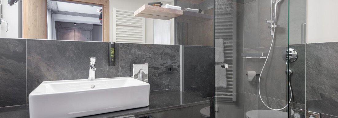 Ein modernes Badezimmer mit einer Glasdusche und einem eleganten Waschbecken. Die Wände sind in dunklen Tönen gehalten, ergänzt durch helles Holz. - AlpenParks The Secret Sölden - Sölden
