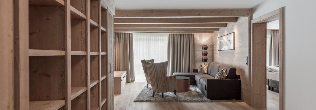 Ein helles und modernes Wohnzimmer mit Holzregalen und einem großen Fenster. Die Einrichtung ist gemütlich und einladend mit einem Sessel und einem Sofa. - AlpenParks The Secret Sölden - Sölden