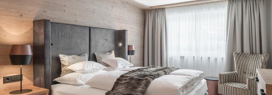 Ein modernes Hotelzimmer mit einem großen Doppelbett und einer bequemen Sitzecke. Große Fenster sorgen für viel natürliches Licht. - AlpenParks The Secret Sölden - Sölden