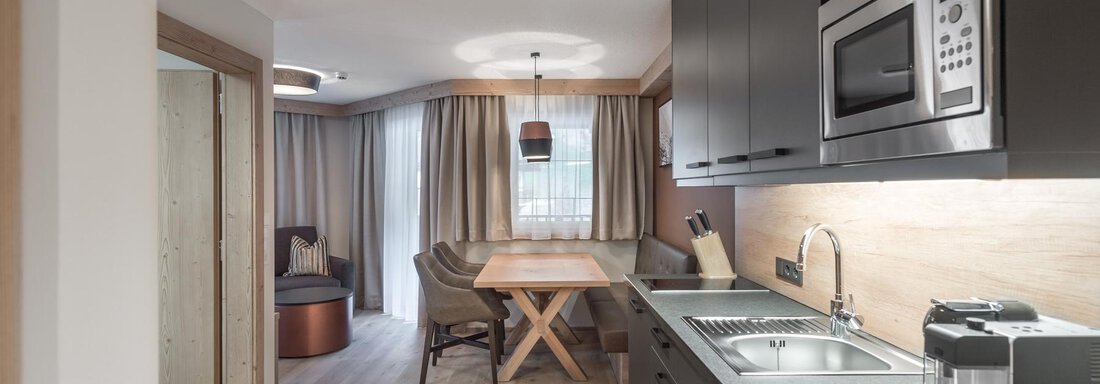 Eine moderne Küche mit einem Esstisch und eleganten Möbeln. Der Raum ist hell und freundlich mit Holz- und Grautönen. - AlpenParks The Secret Sölden - Sölden