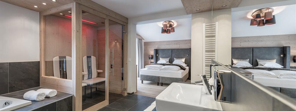 Ein modernes Hotelzimmer mit zwei Betten und eleganter Einrichtung. Die Kombination aus Holz und Stein schafft eine entspannende Atmosphäre, ergänzt durch eine Sauna und ein stilvolles Badezimmer. - AlpenParks The Secret Sölden - Sölden