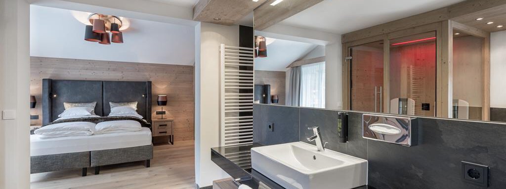 Ein modernes Badezimmer mit einem eleganten Waschbecken und Spiegel. Im Hintergrund sieht man ein gemütliches Schlafzimmer mit einem großen Bett. - AlpenParks The Secret Sölden - Sölden