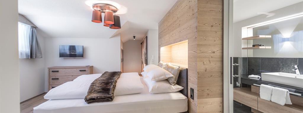 Ein modernes Schlafzimmer mit einem großen Bett und warmen Holzverkleidungen. Es gibt einen Fernseher und ein angrenzendes Badezimmer mit stilvollen Armaturen. - AlpenParks The Secret Sölden - Sölden