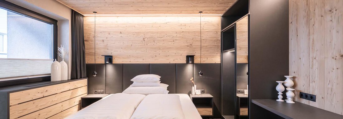 Ein modernes Schlafzimmer mit einem Doppelbett und Holzverkleidung. Sanfte Beleuchtung und stilvolle Möbel schaffen eine gemütliche Atmosphäre. - Apart Reinstadler - Sölden