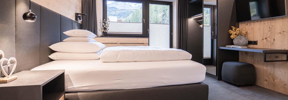 Ein modernes Schlafzimmer mit einem großen Bett und minimalistischer Einrichtung. Große Fenster bieten einen Blick auf die Berge. - Apart Reinstadler - Sölden