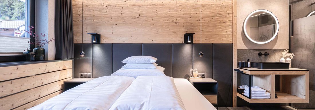 Ein modernes Schlafzimmer mit Holzverkleidung und einer großen Fensterfront. Das Zimmer ist mit einem gemütlichen Doppelbett und eleganten Nachttischlampen ausgestattet. - Apart Reinstadler - Sölden