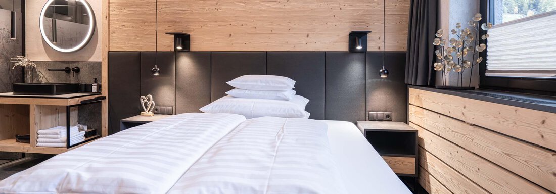 Ein modernes Schlafzimmer mit einem großen Bett und Holzverkleidung. Die sanfte Beleuchtung schafft eine gemütliche Atmosphäre. - Apart Reinstadler - Sölden