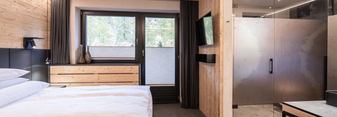 Ein modernes Hotelzimmer mit hölzernen Akzenten und großen Fenstern. Es verfügt über ein bequemes Bett und ein stilvolles Badezimmer. - Apart Reinstadler - Sölden