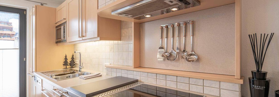 Moderne Küche mit hellen Schränken und einem eleganten Kochbereich. Die Ausstattung umfasst einen Herd und Küchenutensilien an der Wand. - Apart Reinstadler - Sölden