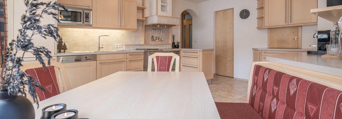 Eine moderne Küche mit hellen Holzmöbeln und einem großen Tisch. Ein gemütlicher Essbereich mit rot-beigen Polstern und dekorativen Vasen. - Apart Reinstadler - Sölden