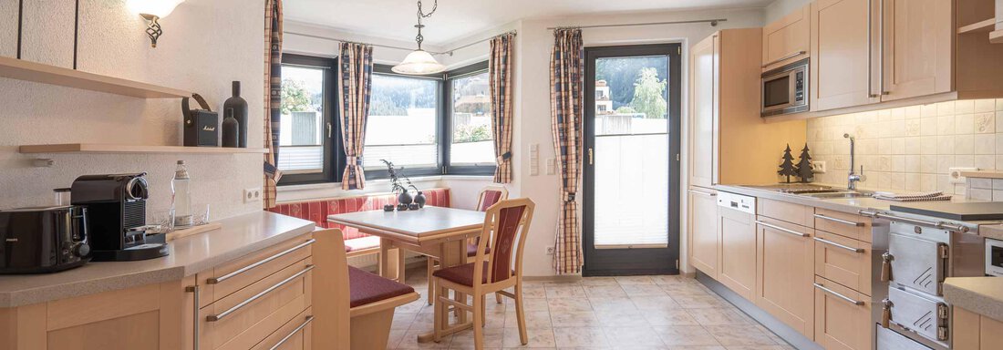 Eine helle und moderne Küche mit Holzschränken und einem Essbereich. Das große Fenster sorgt für viel Tageslicht und Ausblick nach draußen. - Apart Reinstadler - Sölden
