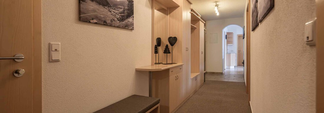 Ein heller Flur mit einem schlichten Holzbank und einigen Wandbildern. Die Wände sind neutral gefärbt und der Boden ist mit Teppich ausgelegt. - Apart Reinstadler - Sölden