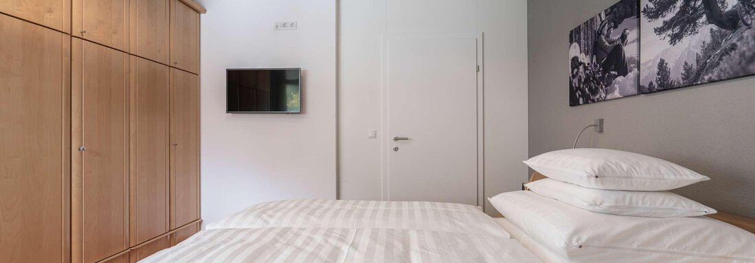 Ein modernes Schlafzimmer mit einem großen Bett und weißen Bettwaren. An der Wand befindet sich ein Fernseher und ein Kleiderschrank aus Holz. - Apart Reinstadler - Sölden