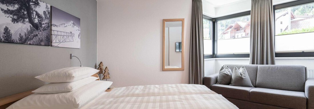 Ein helles Hotelzimmer mit zwei Einzelbetten und einem gemütlichen Sofa. Große Fenster bieten viel Tageslicht und einen Blick auf die Umgebung. - Apart Reinstadler - Sölden